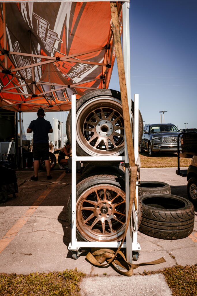 Tires on a rack under a tent at a car racing track, captured outdoors.